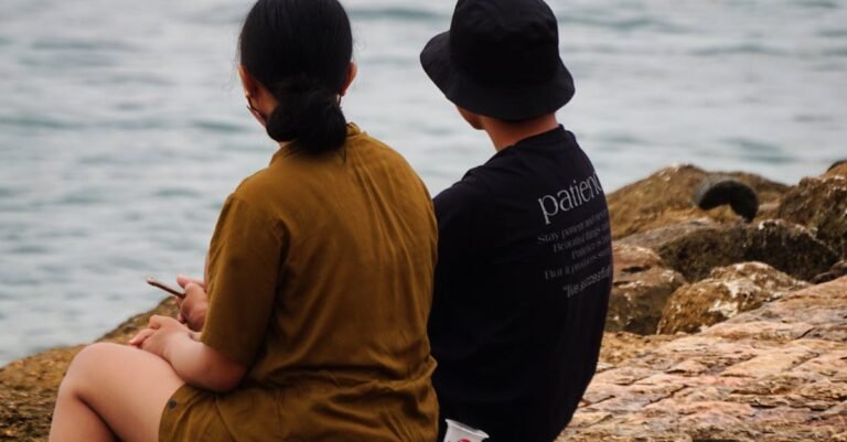A couple enjoys a tranquil moment sitting on rocks at Sanur Beach, Bali, with the sea in the background.